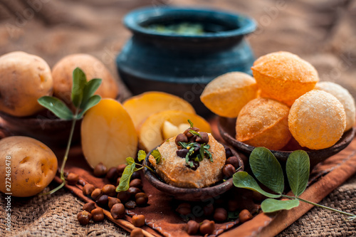 Famous Indian & Asian street food dish i.e. Panipuri snack in a clay bowl along with its flavored spicy water in another clay vessel. Entire consisting raw ingredients present on the surface. photo