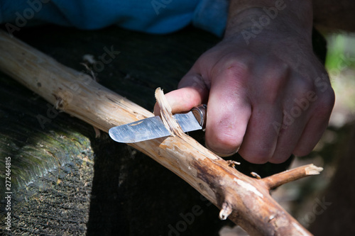Man creating a walking stick with a knife