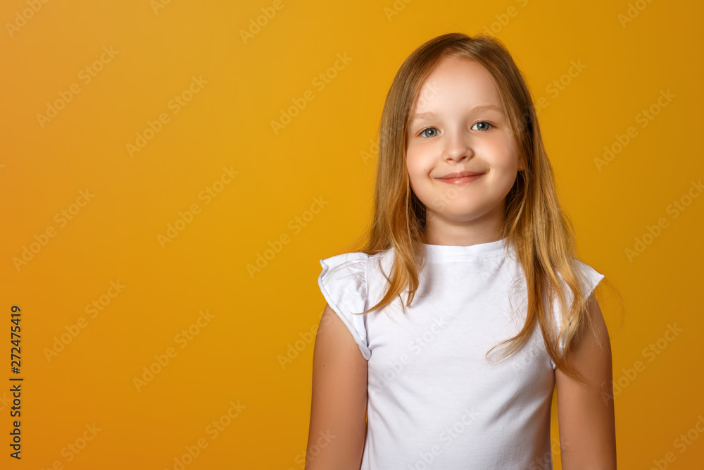 Portrait of a cute little girl on a yellow background. A child blonde is smiling and looking at the camera. Copy space. - obrazy, fototapety, plakaty 