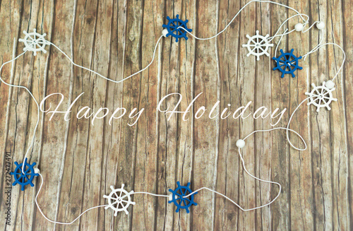 Maritime decoration with blue and white steering wheels on wood background, in the middle the words happy holiday