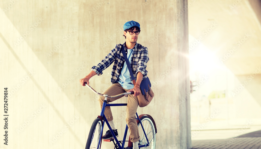 Obraz premium people, style, leisure and lifestyle - young hipster man with shoulder bag riding fixed gear bike on city street