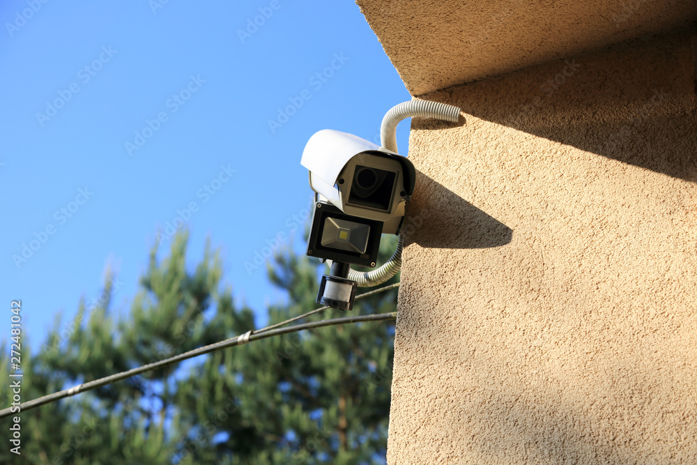 Kamera monitoringu z reflektorem led i czujnikiem ruchu na ścianie budynku. - obrazy, fototapety, plakaty 