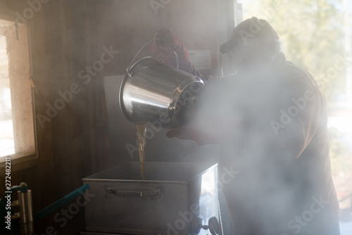 Maple syrup farmer processes fresh natural syrup in steamy sugar shack