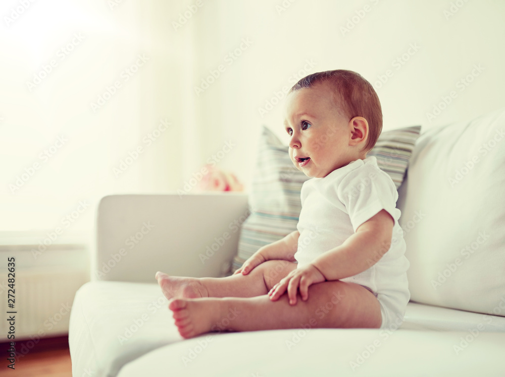 childhood, babyhood and people concept - happy little baby boy or girl sitting on sofa at home childhood, babyhood and people concept - happy little baby boy or girl sitting on sofa at home