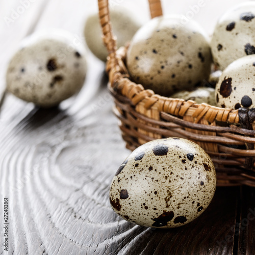Fresh organic quail eggs in small wicker basket on rustic kitchen table. Space for text