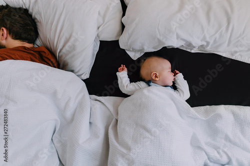 A baby boy asleep in a big bed with his Dad co-sleeping by his side
