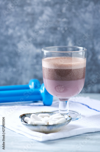 Glass of Chocolate Protein Shake with milk and black currant . L - Carnitine and blue dumbbells in background. Sport nutrition. Wooden background. Copy space.  photo