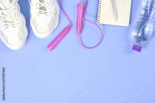 Sports equipment. Skipping rope, sneakers, bottle water, pen and notepad on purple background. Fitness and healthy lifestyle concept.Flat lay, top view, copy space