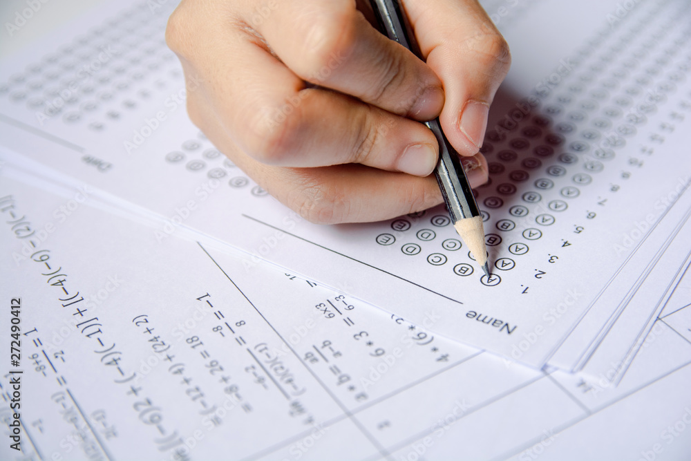 Students hand holding pencil writing selected choice on answer sheets and Mathematics question sheets. students testing doing examination. school exam Students hand holding pencil writing selected choice on answer sheets and Mathematics question sheets. students testing doing examination. school exam