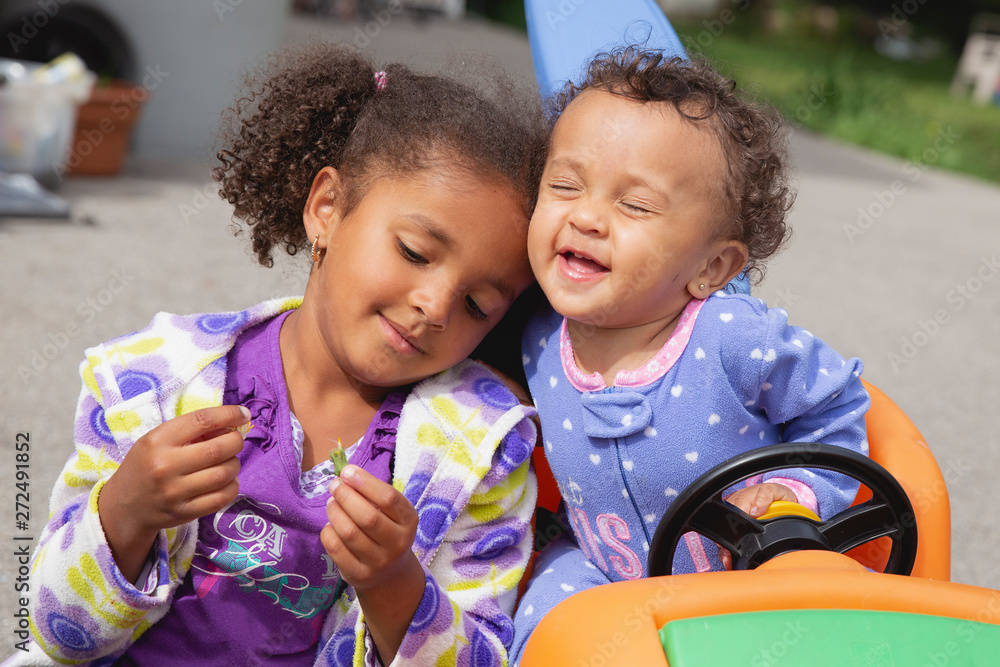 Portrait of two sisters sitting together in the driveway of their home Portrait of two sisters sitting together in the driveway of their home
