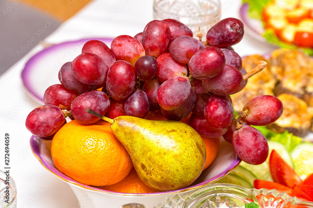 Fruit in a plate on the table. Bunch of grapes, pear and orange on the plate Fruit in a plate on the table. Bunch of grapes, pear and orange on the plate