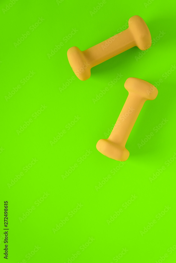 Fitness equipment with womens yellow weights/ dumbbells isolated on a lime green background with copyspace Fitness equipment with womens yellow weights/ dumbbells isolated on a lime green background with copyspace