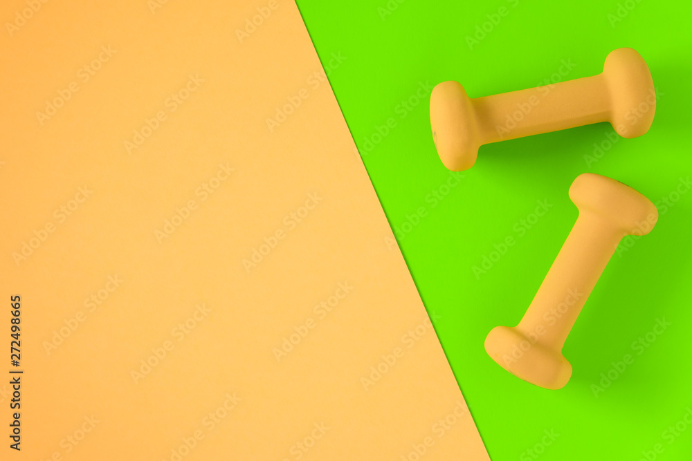 Fitness equipment with womens yellow weights/ dumbbells isolated on a lime green and yellow pink background with copyspace Fitness equipment with womens yellow weights/ dumbbells isolated on a lime green and yellow pink background with copyspace