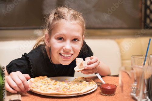 Young teenage girl in the cafe eats tasty pizza and smiles. The girl loves pizza and often goes to the pizzeria