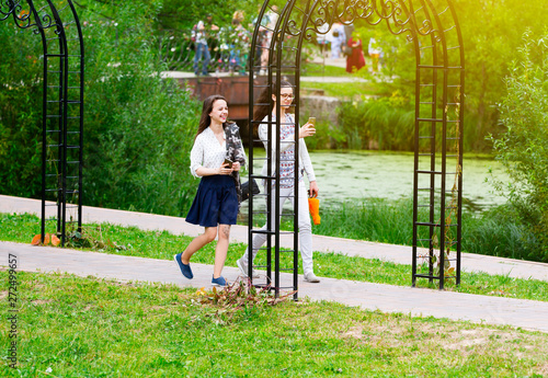 full length two friends having walk in a park in Russian traditional park in Moscow. young girls communicating and using mobile phones by nature pool. women travelers browse map app