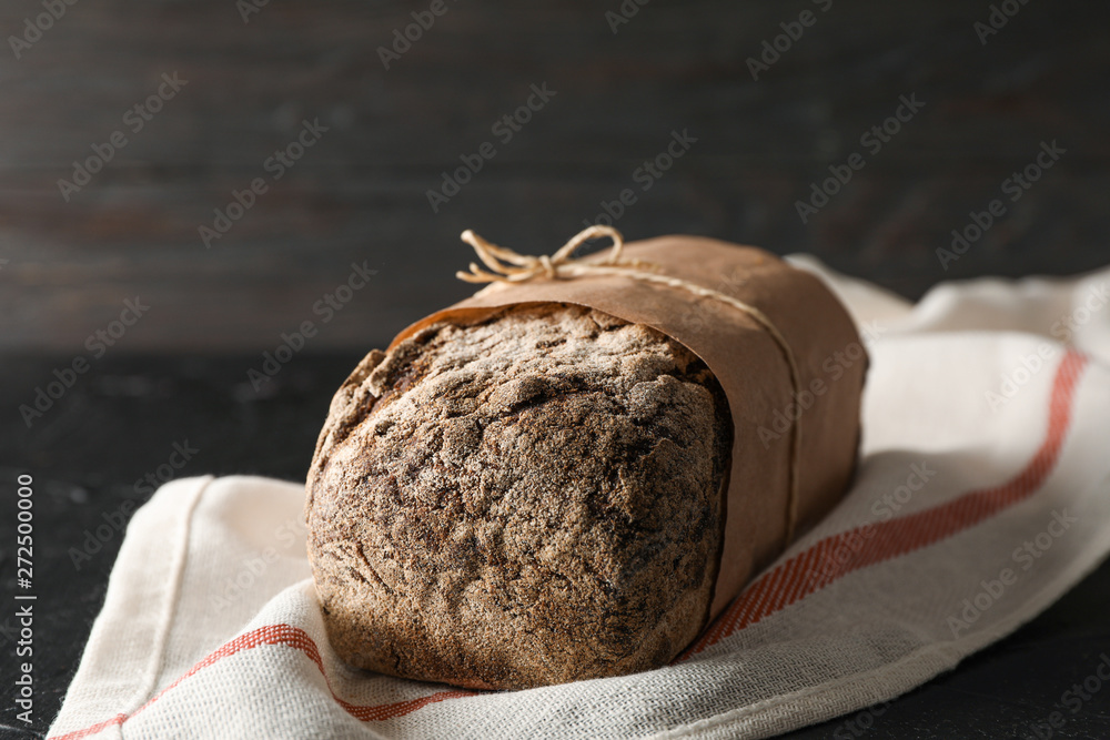 Rye bread on kitchen towel on black table against wooden background, space for text and closeup