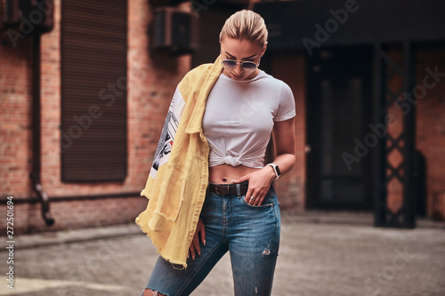 Cheeky trendy woman in sunglasses is posing for photographer at random city yard. photo