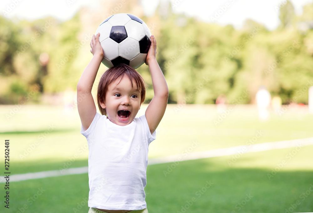 Excited little toddler boy playing football on soccer field outdoors