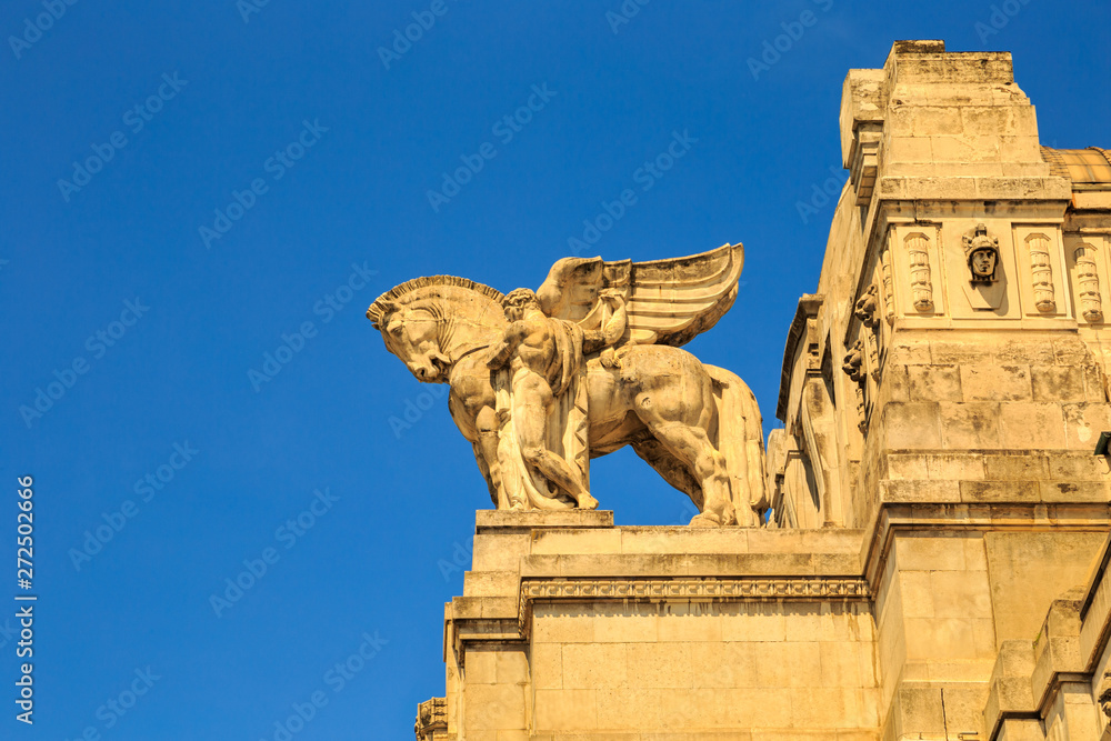 Winged horse (pegasus) ornament on top of a historical stone building of main train station (Milano Centrale) in Milan, Italy. Sunny day with clear blue sky.