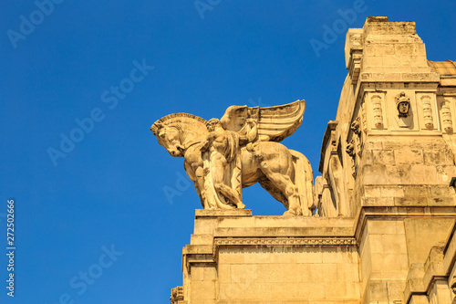 Winged horse (pegasus) ornament on top of a historical stone building of main train station (Milano Centrale) in Milan, Italy. Sunny day with clear blue sky. © Predrag Jankovic