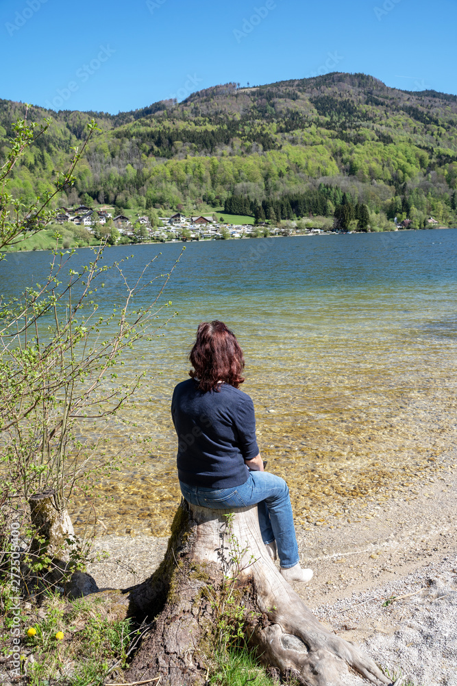 Fototapeta premium Junge Frau sitzt auf einem Baumstumpf am See