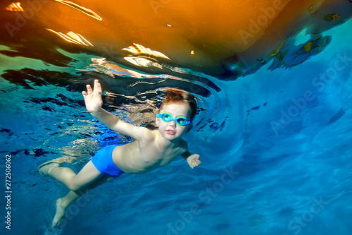 A little boy swims underwater in the pool near the surface of the water. Portrait. Underwater photography. Blue background. Horizontal orientation
