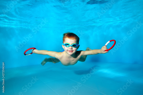 Sporty little boy swimming underwater in the pool with toys in his hands. Portrait. Close up. Underwater photography. Horizontal orientation photo