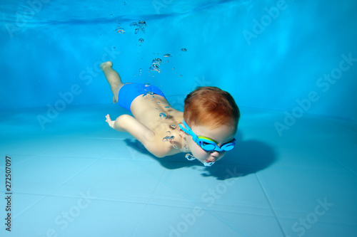 Little sports boy swims under water,dives to the bottom of the pool. Blowing bubbles underwater. Portrait. Photo under water. Horizontal orientation