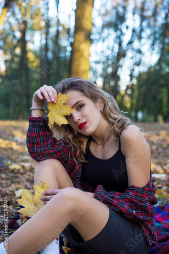 Beautiful Autumn Woman with Autumn Leaves on Fall Nature Background. Cute teenage student girl in shirt in the cell.
