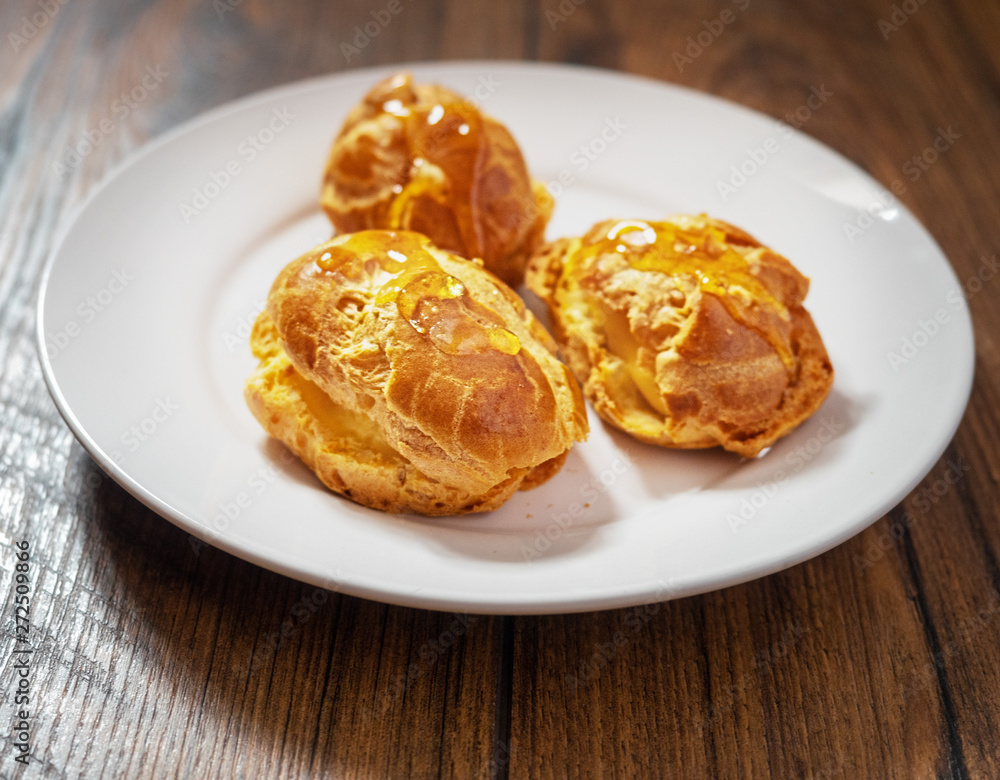 Three cream puffs on a white plate filled with custard and topped with sweet syrup.
