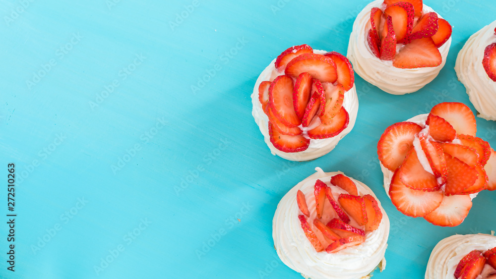 A small meringue Pavlova dessert with some strawberry slices on a blue background. Top view. A small meringue Pavlova dessert with some strawberry slices on a blue background. Top view.