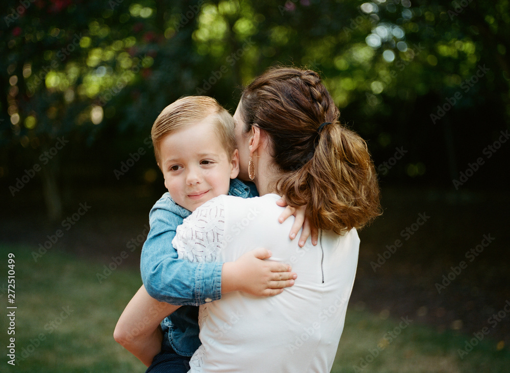 Adorable young boy peeking over the shoulder of his mother Adorable young boy peeking over the shoulder of his mother