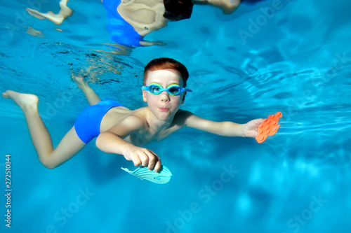 Little sports boy swims underwater,dives to the bottom of the pool with toys in . Posing for the camera with his eyes open. Portrait. Photo underwater. Horizontal orientation