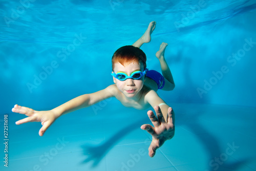 Cute sports boy swimming underwater in the pool. Posing for the camera with glasses. Bottom view from the bottom of the pool. Portrait. Underwater photography. Horizontal view