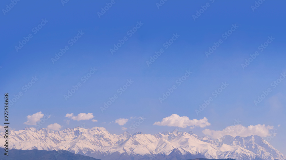 Panorama of mountain peaks, in a haze of clouds, from a bird's flight, against a blue sky, lit by the sun