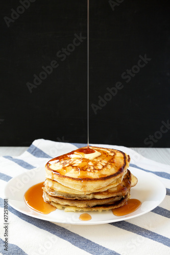 Homemade pancakes with butter and maple syrup on a white plate, side view. Close-up.