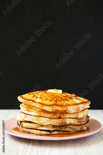 Homemade pancakes with butter and maple syrup on a pink plate, side view. Closeup.