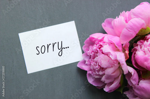 sorry card message on white postcard and pink flowers Flatley style decoration on grey background.
