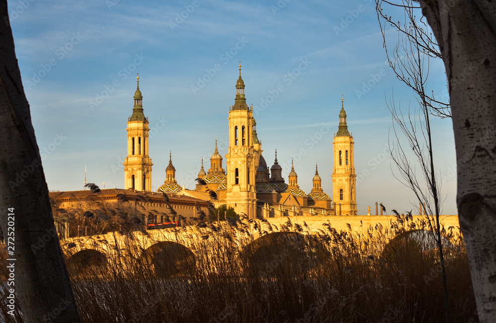 landscape of a sunrise on catholic basilica pilar in Zaragoza besides the Ebro river with some trees and plants at first site. The bridge over the Ebro river is called the stone bridge. Horizontal