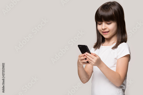 Little girl using smartphone standing aside isolated on grey background