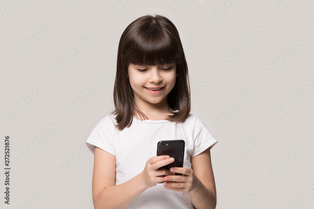 Little girl using smart phone posing isolated on grey background Little girl using smart phone posing isolated on grey background