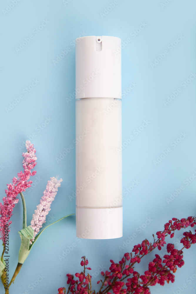 Flat lay composition with cosmetic products, mockup white tubes and red flowers on a blue background Flat lay composition with cosmetic products, mockup white tubes and red flowers on a blue background