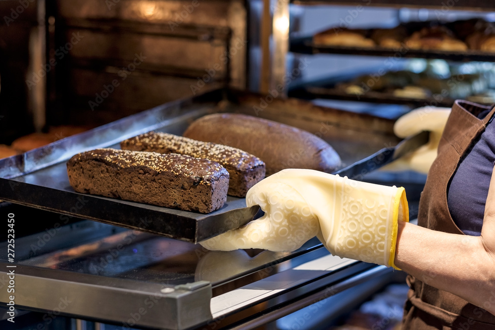 young baker on rubber gloves holding a tray with fresh bread taking them  out of oven. Stock Photo | Adobe Stock