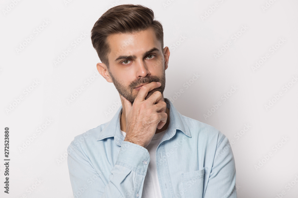 Thoughtful young man holding hand on chin feeling doubtful Thoughtful young man holding hand on chin feeling doubtful