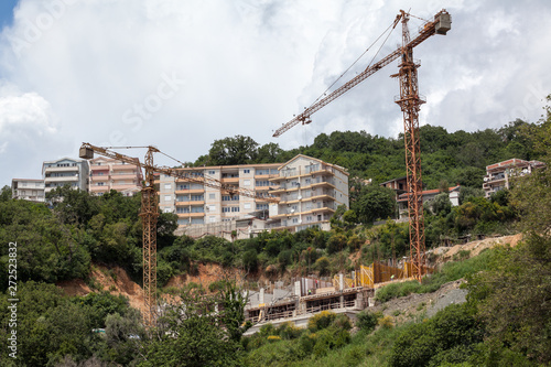 Construction site of public buildings on hills near sea coastline. Cranes during lifting operations