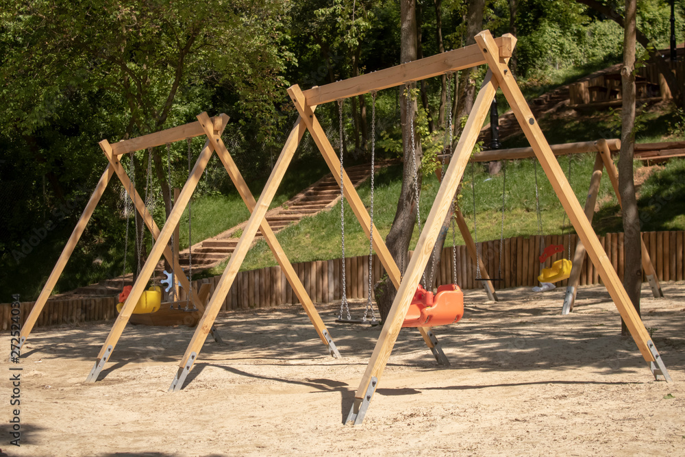 Fototapeta premium Playground swing. Wooden poles and plastic seats. Trees in the background