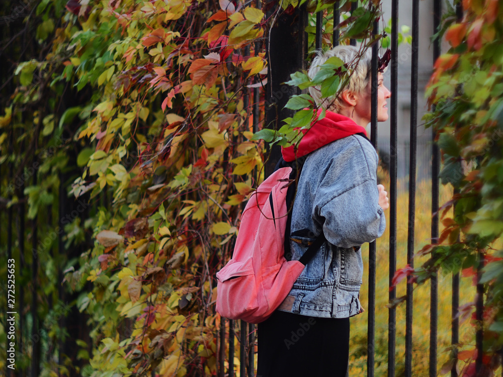 A young girl looks through a fence covered with autumn leaves A young girl looks through a fence covered with autumn leaves