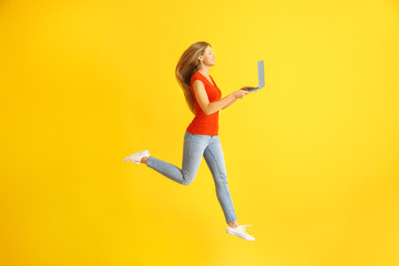 Beautiful jumping woman with laptop on color background