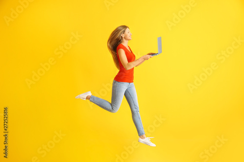 Beautiful jumping woman with laptop on color background