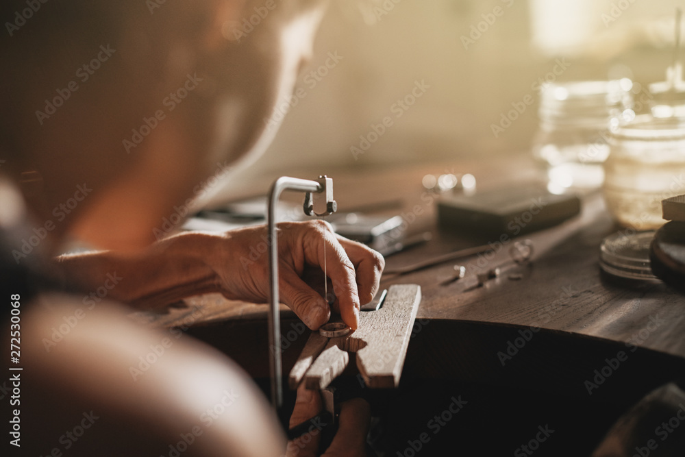 Female jeweler using her saw to shape a ring Female jeweler using her saw to shape a ring